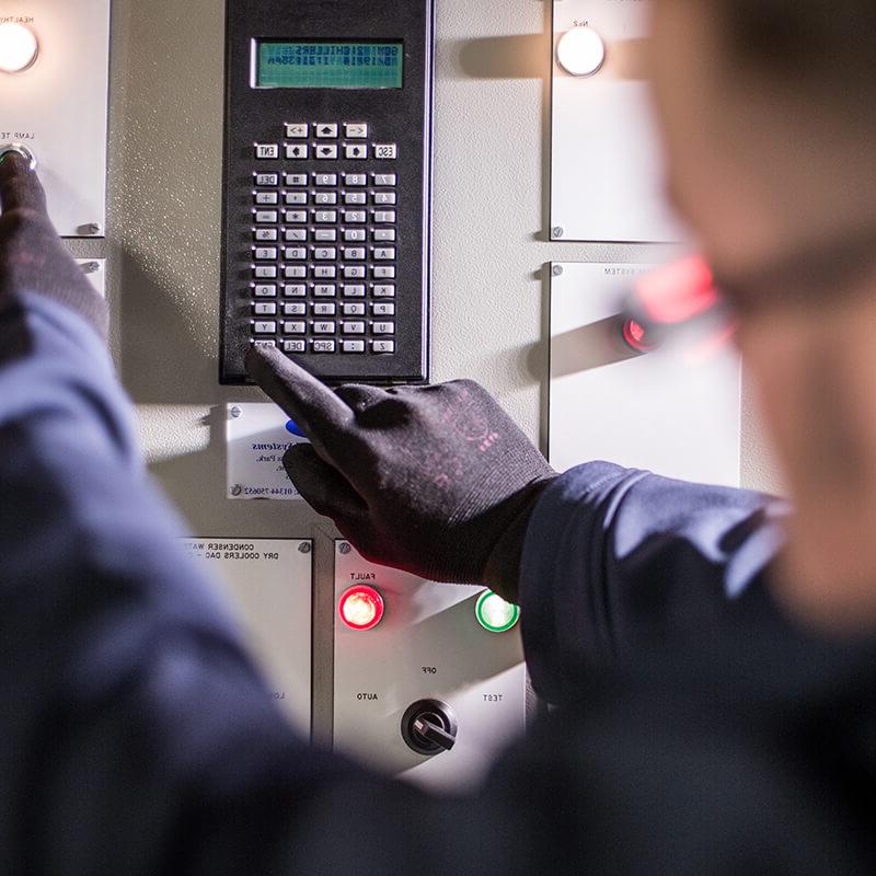 关闭 up of a Mitie engineer wearing black gloves pressing buttons on a control panel